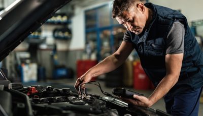 Car mechanic analyzing amperage of car battery in a repair shop. Auto mechanic using diagnostic tool while checking car battery voltage in a workshop.
